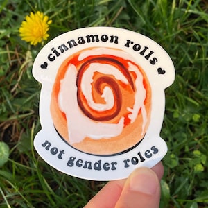 May include: White sticker with a cinnamon roll illustration and the text "cinnamon rolls not gender roles" in black.