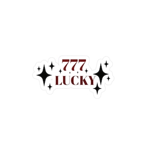 以下が含まれることがあります： 白地に、バーガンディ色の「777 LUCKY」の文字と黒い星が描かれたステッカー。光沢のある仕上がりで、装飾目的で使用されることを意図しています。