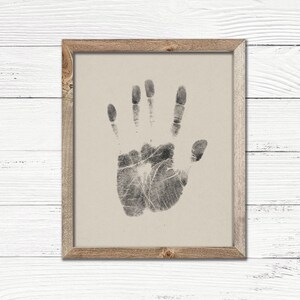 May include: A framed print of a black handprint on a beige background. The handprint is of a left hand with all five fingers extended.