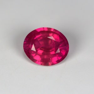 Puede incluir: Una gema ovalada de color rojo intenso y vibrante, con un corte facetado.