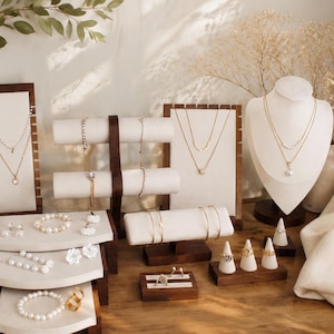 May include: A display of various gold and pearl jewelry pieces. Necklaces, bracelets, and rings are showcased on wooden stands and display forms. The jewelry includes delicate chains, pearl strands, and rings with floral and gemstone accents.
