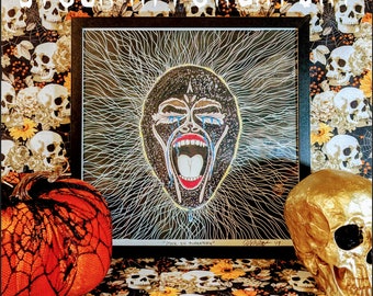 May include: A framed black and white illustration of a screaming face with blue tears. The frame is on a table with a pumpkin and a gold skull. The background is a black and white pattern of skulls and flowers.
