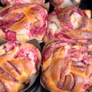 Könnte beinhalten: Nahaufnahme von frisch gebackenen, gewirbelten Brötchen mit einer leuchtend roten Füllung, eingebettet in Papierformen in einem Backblech. Die goldbraunen Oberseiten kontrastieren mit dem farbenfrohen Inneren und deuten auf ein süßes Gebäck hin.