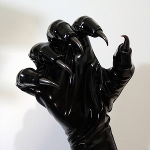 May include: Black leather gloves with long claws. The gloves are shiny and have a textured surface.