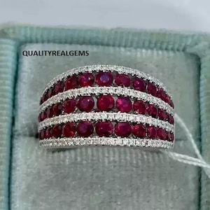 May include: A wide band ring with four rows of red ruby stones set in a white metal band. Each row of rubies is separated by a row of smaller white diamonds.