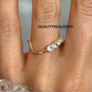 Può includere: Un anello color oro con cinque gemme trasparenti incastonate in un design curvo. L'anello è su un dito, e il testo "QUALITYREALGEMS" è visibile.
