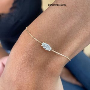 Op de afbeelding: Een delicate gouden kettingarmband met een enkele ovale diamant. De armband wordt getoond op de pols van een persoon.