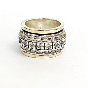 May include: A silver and gold ring with a spinning band of clear stones. The ring is set with a row of small, clear stones around the band.