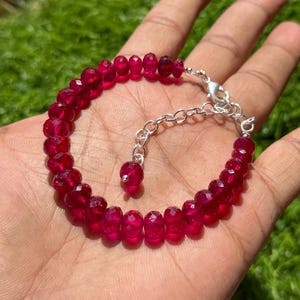 May include: A red gemstone bracelet with a silver clasp and extender chain. The bracelet is made of faceted beads and is approximately 7 inches in length.