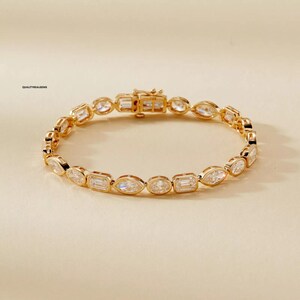 Puede incluir: Un brazalete de oro con una fila de piedras ovaladas transparentes y facetadas. El brazalete tiene un cierre.
