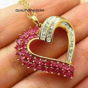 May include: A gold-toned heart pendant necklace. The pendant features a heart shape with a section of small, round, pink gemstones and a section with small, clear gemstones. The necklace chain is also gold-toned. The text "QUALITYREALGEMS" is visible.