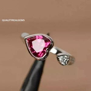 Puede incluir: Un anillo de plata con una piedra preciosa rosa en forma de corazón y una piedra preciosa transparente más pequeña en el lateral.