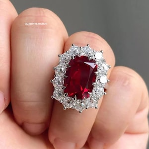 Peut inclure: Une bague en argent avec une pierre rouge centrale entourée d'un halo de petites pierres blanches.