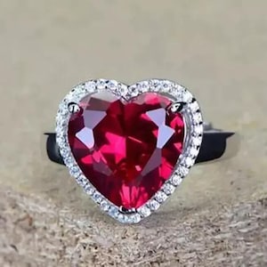 Puede incluir: Un anillo de plata con una gran piedra de rubí en forma de corazón rodeada por un halo de piedras blancas más pequeñas.