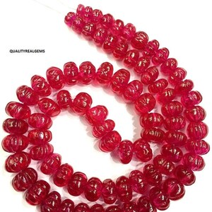 May include: A strand of bright red ruby beads, each bead is carved with a flower-like design. The beads are strung on a thin wire and are arranged in a circular pattern.