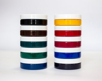 May include: Two stacks of paint pots, one with black, brown, green, and blue paint, and the other with yellow, red, purple, blue, and black paint.