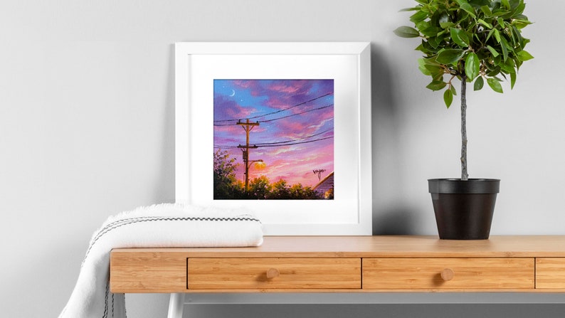 May include: A framed painting of a sunset with a crescent moon in the sky. The painting features a wooden utility pole with power lines and a streetlight. The sky is a vibrant mix of pink, purple, and orange.