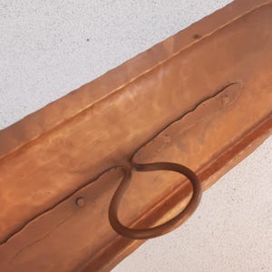 May include: A copper wall mounted shelf with a single hook. The shelf is rectangular and has a hammered finish. The hook is a simple loop.