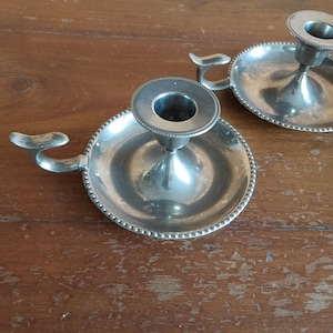 Può includere: Due portacandele d'argento con un bordo decorato a perline. Ogni portacandele ha una base rotonda e un'unica coppa per candele.