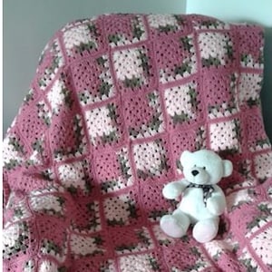 Puede incluir: Una manta de crochet rosa, blanca y verde con un oso de peluche blanco sentado encima. La manta está hecha con un patrón cuadrado y tiene el título "The Mitered Throw".