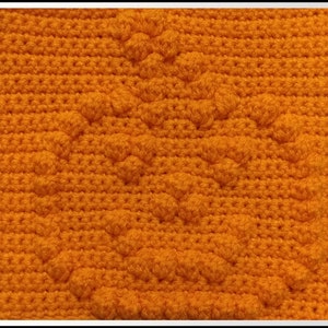 Op de afbeelding: Close-up van een gehaakt stof met een textuurpatroon. De stof is fel oranje van kleur en heeft een herhalend patroon van kleine bultjes.
