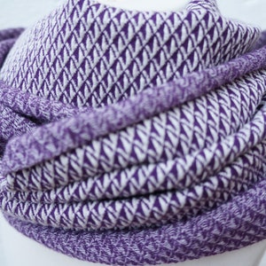 Könnte beinhalten: Ein lila-weißer Infinity-Schal mit Chevron-Muster. Der Schal ist aus weichem, gestricktem Stoff.