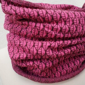 Könnte beinhalten: Ein rosa gestrickter Halsschmuck mit einem Blatt-Muster. Der Halsschmuck ist gefaltet und hat einen dunkelrosa Saum.