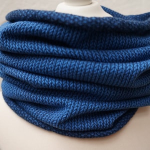 May include: A blue knitted neck warmer or cowl, folded and displayed on a white mannequin.