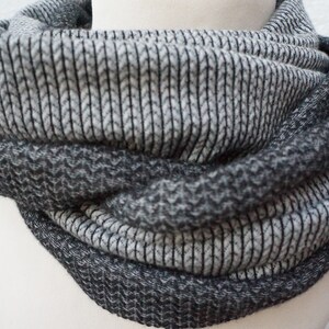 Könnte beinhalten: Ein grauer und schwarzer Infinity-Schal aus weichem, strukturiertem Stoff. Der Schal ist in der Mitte gefaltet und hat ein Rippenmuster.