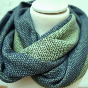 Könnte beinhalten: Blau-grüner Loop-Schal mit strukturiertem Webmuster. Der Schal ist um einen weißen Schaufensterkopf drapiert und zeigt sein Design und seine Farbvariationen. Der Stoff wirkt weich und bequem, ideal für kühleres Wetter.