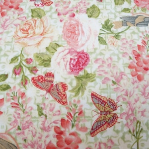 Könnte beinhalten: Ein weißer Stoff mit einem floralen Muster mit rosa und roten Rosen, grünen Blättern und Schmetterlingen. Der Hintergrund ist hellgrün mit einem dezenten Gittermuster.