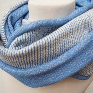 Könnte beinhalten: Ein blauer und weißer Infinity-Schal mit einem strukturierten Strickmuster. Der Schal ist in der Mitte gefaltet und wird auf einer weißen Puppe präsentiert.