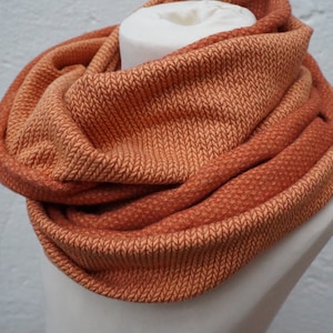 Könnte beinhalten: Ein warmer orangefarbener und pfirsichfarbener Infinity-Schal aus weichem, gestricktem Stoff.