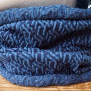 Könnte beinhalten: Ein blauer Strickschal mit strukturiertem Muster. Der Schal hat einen tiefen Blauton mit einem helleren blauen Muster. Der Schal ist mehrfach gefaltet, wodurch die Textur und Dicke des Strickstoffs sichtbar wird.