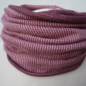 Könnte beinhalten: Ein gestrickter Rundschal in Rosa- und Lilatönen, auf einer Schaufensterpuppe präsentiert. Der Rundschal hat ein strukturiertes Rippenmuster mit dunklerem lila Besatz. Der Stoff wirkt weich und warm, geeignet für kaltes Wetter. Der Rundschal ist ein Halstuch.