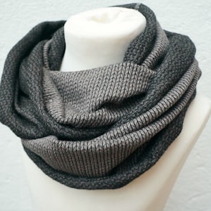 Könnte beinhalten: Ein grauer und schwarzer Infinity-Schal aus weichem, gestricktem Stoff. Der Schal ist zu einer Schleife gefaltet und wird auf einem weißen Mannequin präsentiert.
