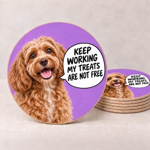 May include: A round coaster featuring a brown curly-haired dog on a purple background. A white speech bubble contains the black text: KEEP WORKING MY TREATS ARE NOT FREE. A stack of identical coasters is visible to the right of the main coaster.