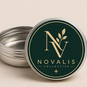 May include: A small, open, silver tin with a dark green lid. The lid displays a gold logo with the text "NOVALIS COLLECTIVE". The logo includes the letters "N" and "V" with a leaf design.