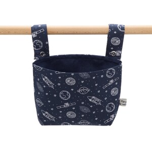 May include: A navy blue hanging organiser with a white space-themed print featuring planets, stars, rockets, and a satellite. The organiser has two loops for hanging and a label that reads "Mary & the Bubble".