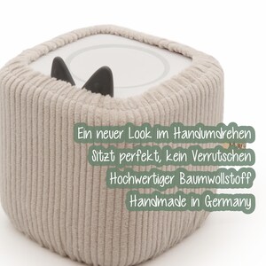 May include: A beige corduroy fabric cover for a square object, with two black, ear-shaped accents peeking out from the top. The text on the image reads: "A new look in an instant, fits perfectly, does not slip, high-quality cotton fabric, handmade in Germany."