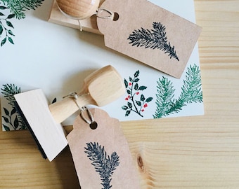 May include: Wooden stamps with fir tree designs, paired with matching kraft paper tags and stationery. The stamps have wooden handles and are used to create a festive, nature-inspired aesthetic. The stationery features green and red accents.