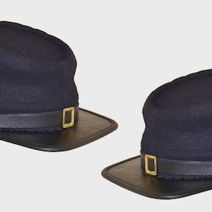 Puede incluir: Dos gorras kepi azul marino de la Guerra Civil. Cada sombrero tiene una visera de cuero negro, una correa de barbilla de cuero negro con una hebilla dorada y un botón dorado. Los sombreros son de estilo militar histórico.