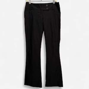 May include: Solid black trousers featuring a wide waistband with two visible buttons at the center front. These pants have a straight-leg cut, a clean finish, and are suspended from a metal hanger, showing a simple and functional design.
