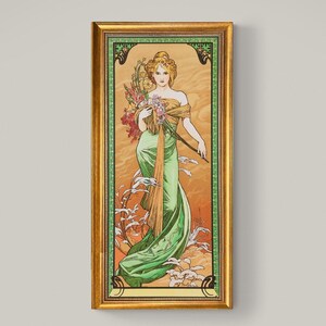 May include: A framed art print depicting a woman in a green dress holding flowers. The artwork is in a gold frame with green and gold detailing. The background is a warm orange and tan colour.