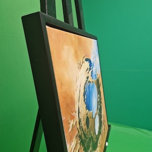 Könnte beinhalten: Ein gerahmtes abstraktes Gemälde mit einem schwarzen Rahmen. Das Gemälde zeigt ein wirbelndes Muster in Blau, Weiß und Braun.