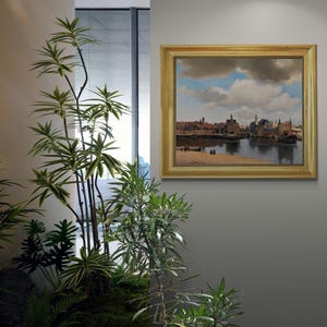 a framed painting of a cityscape with a river in the background, hanging on a wall next to a potted plant.