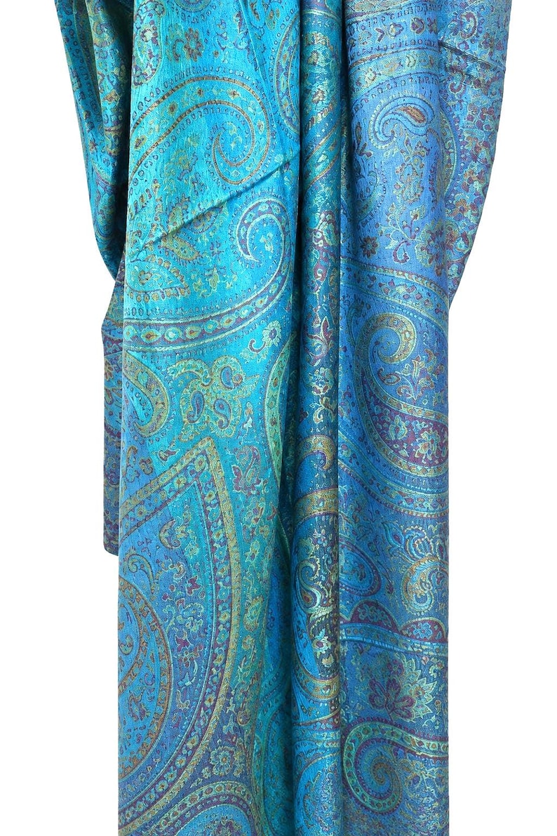 May include: A vibrant turquoise scarf featuring an intricate, repeating paisley pattern in shades of deep blue, purple, and metallic gold. The fabric displays a subtle sheen and a complex, dense design of swirling teardrop motifs and floral elements.