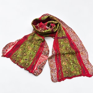 Könnte beinhalten: Ein langer, rechteckiger Schal mit knittriger Textur in einer lebendigen Farbpalette aus Limettengrün, Dunkelrot und Creme. Der Stoff zeigt ein komplexes Muster aus floralen Motiven und geometrischen Bordüren mit verschiedenen Paneelen.