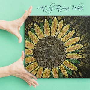 Könnte beinhalten: Eine Nahaufnahme eines Sonnenblumenbildes auf Leinwand. Die Sonnenblume besteht aus kleinen gelben und orangefarbenen Punkten mit einer braunen Mitte. Der Hintergrund ist schwarz mit goldenen Akzenten.