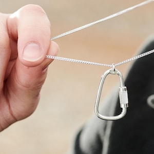 Peut inclure: Un collier en argent avec un pendentif en forme de mousqueton. Le pendentif est un petit mousqueton en argent avec un anneau texturé.